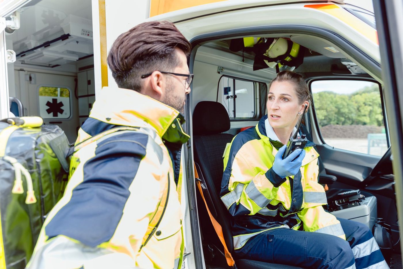 A paramedic in the cab of her ambulance talks on a portable radio while her partner listens.