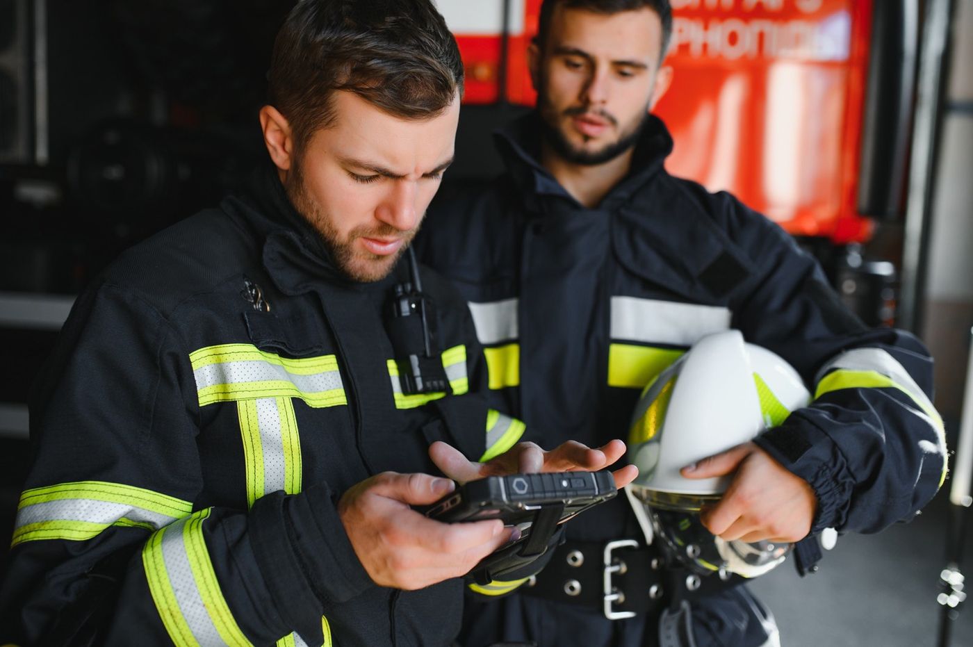 Two firefighters in turnout gear check a rugged tablet in front of their engine.